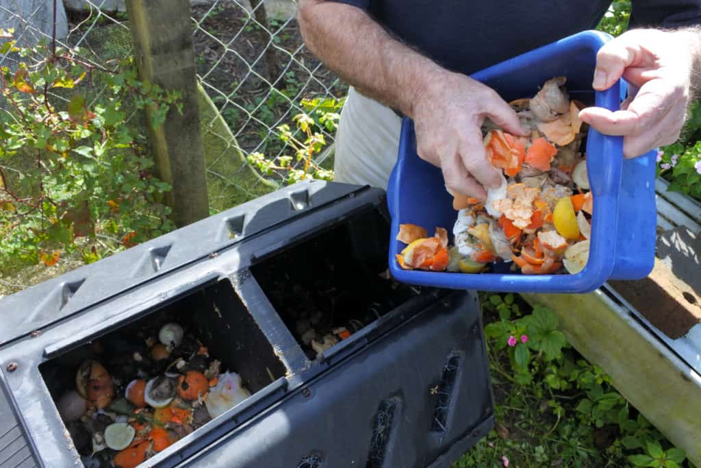 Man adding food scraps into a popular style of compost bin, a compost tumbler