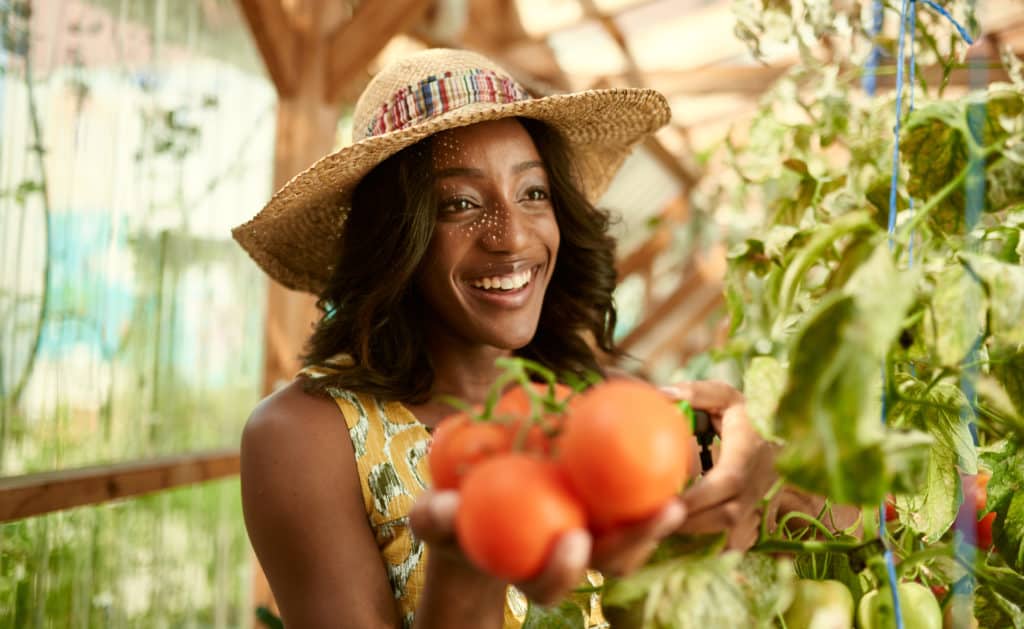 Woman in a hat smiling with homegrown tomatoes