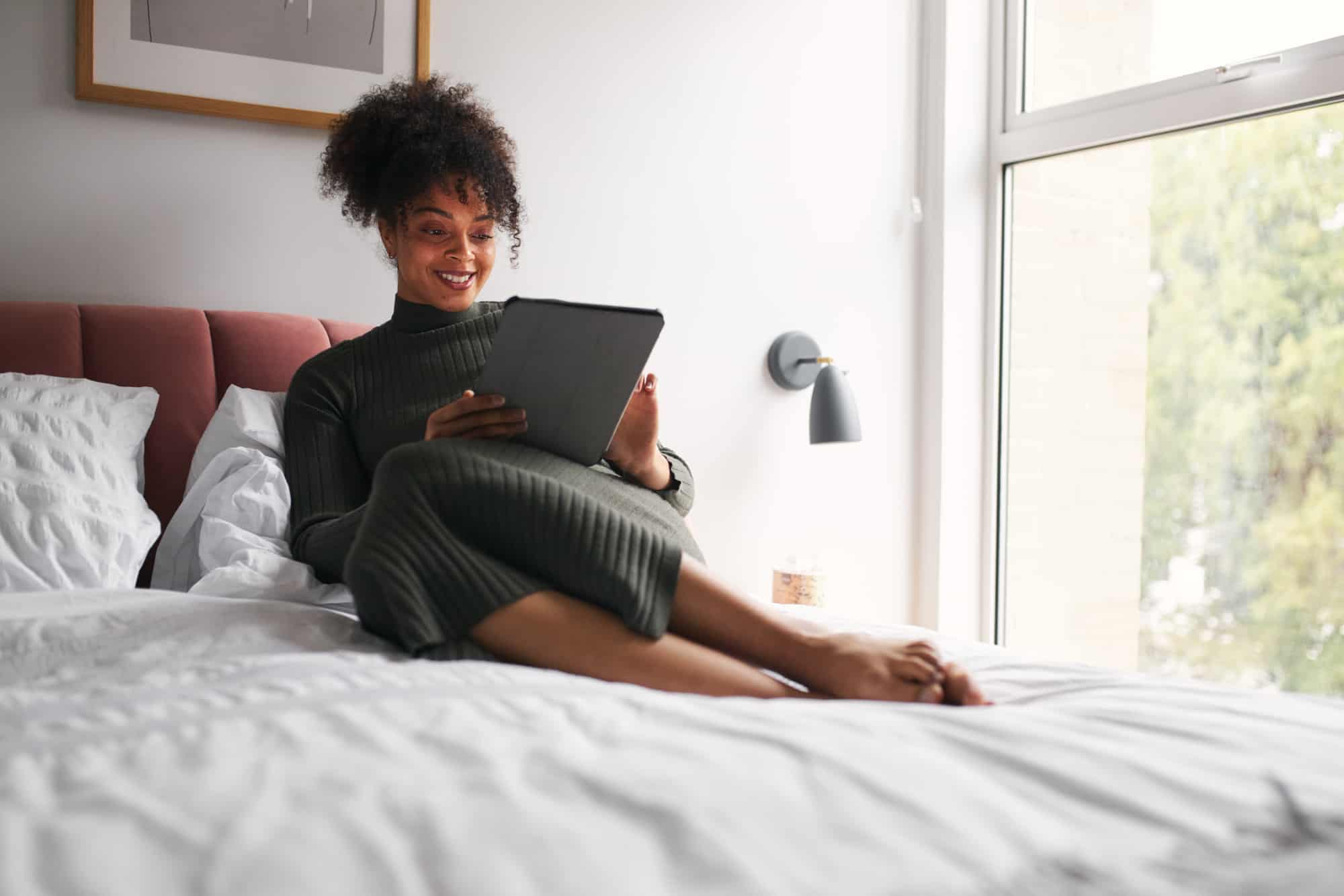 Woman reading ebooks on a tablet while siting on her bed